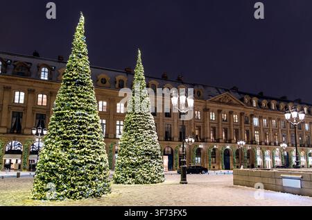Illuminated Christmas trees standing in snow on Place Vendome in Paris at night surrounded by historic architecture. Stock Photo