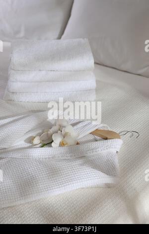 Clean bathrobe, towels and flowers on bed indoors, closeup Stock Photo