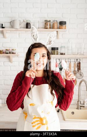 Beautiful funny brunette woman in red sweater and white apron wearing rabbit ears, covering eyes with easter eggs decorations Stock Photo
