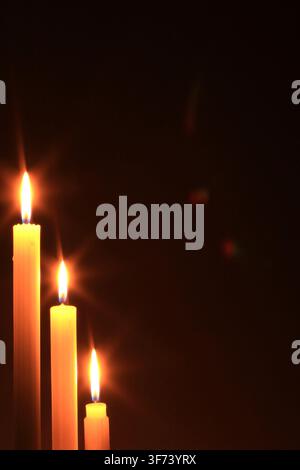 Three candles alight in the dark, with starburst flames on the diagonal, and with subtle lens flare, all against a rich brown gradient background. Stock Photo