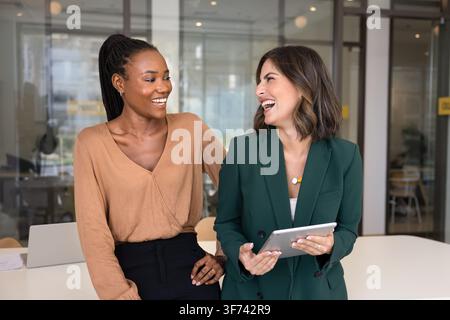 Happy female colleagues sharing ideas and laughing at workplace Stock Photo