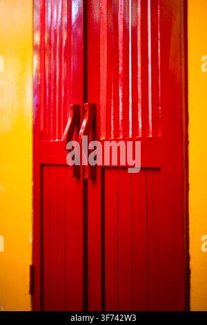 Red wooden double doors with handles on yellow wall at vintage building in Hoi An city Vietnam. Stock Photo