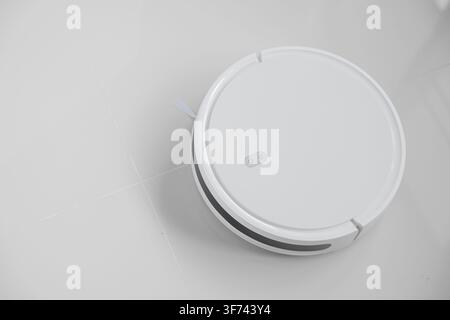 White automatic floor cleaner with side brush on tile flooring, designed for efficient cleaning. Robot vacuum concept of smart home technology for sea Stock Photo