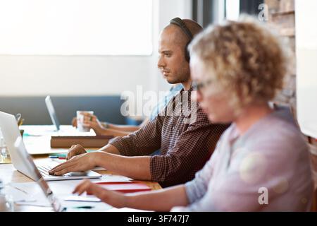 Man, headphones and typing in office with laptop, software development and listen to music playlist. Coworking, person and computer programming in Stock Photo