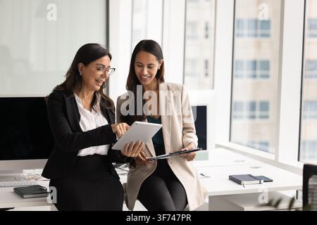 Smiling diverse business team members discussing work result or online project data, collaborating on joint tasks, reviewing information on digital ta Stock Photo