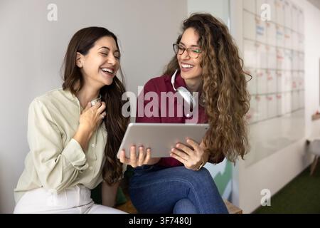 Two female coworkers laughing during collaborative meeting using digital tablet Stock Photo