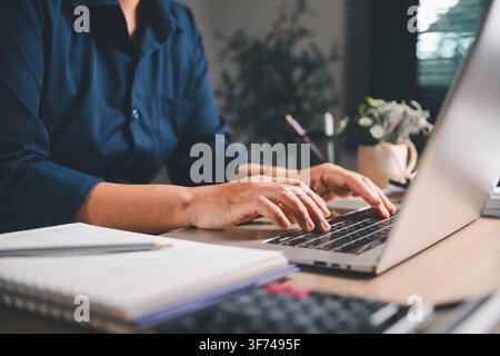 Close-up of a business professional typing on a laptop beside a notebook and calculator, representing remote work, online business, data entry, digita Stock Photo