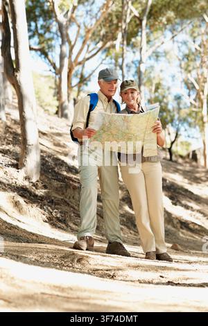 Map, hiking and reading with old couple in nature for trekking, fitness and adventure guide. Wellness, retirement vacation and location search with Stock Photo