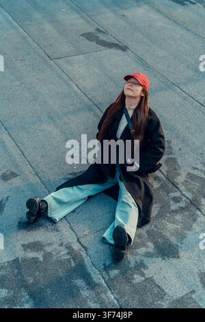 Woman sitting cross-legged on rooftop floor, high angle view, Qingdao, China Stock Photo