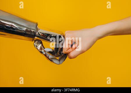 A human hand and a robotic hand engage in a symbolic handshake against a bright yellow background, representing the intersection of humanity and technology. Human and Robot Handshake Stock Photo