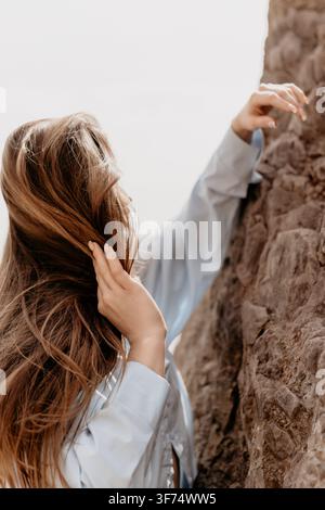Woman hair nature scene featuring a young female touching a rocky cliff outdoors during bright day with copy space Stock Photo