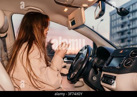 Woman car sunset Young woman sitting in driver seat holding e-cigarette device in vehicle interior during golden hour Stock Photo