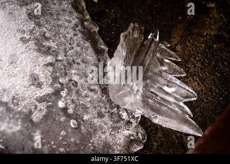 Macro photography of sharp frozen ice fragments resting on a textured dark ground surface small air bubbles and translucent crystal structures capturi Stock Photo