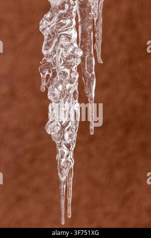 Sharp frozen icicles hanging against a textured brown background translucent ice formations with intricate details created by freezing water patterns Stock Photo