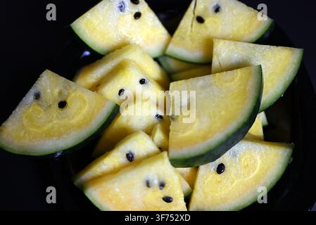 Yellow watermelon cut into triangles on black background Stock Photo