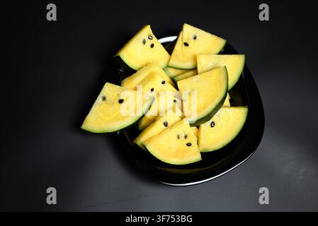 Yellow watermelon cut into triangles on black background Stock Photo
