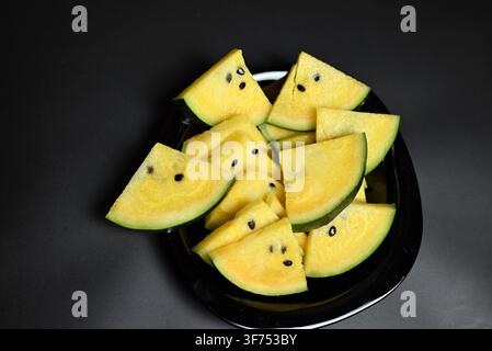 Yellow watermelon cut into triangles on black background Stock Photo