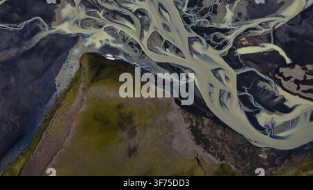 Overhead aerial perspective of glacial outwash plain featuring braided meltwater streams with pale sediment-laden water against dark. Stock Photo