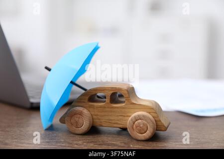 Insurance. Toy car with small umbrella on wooden table indoors, closeup Stock Photo