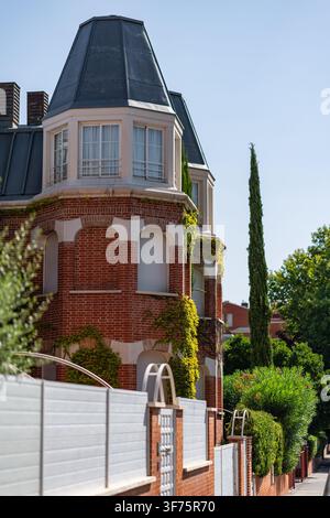 Corner of red brick residence with projecting dormer windows mansard roof and tall cypress tree Stock Photo
