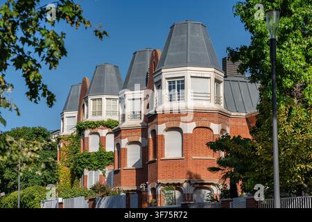 Row of red brick residential buildings with gray mansard roofs framed by mature green trees Stock Photo