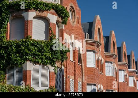Decorative red brick facades with repeating gables shuttered windows and thick climbing ivy Stock Photo