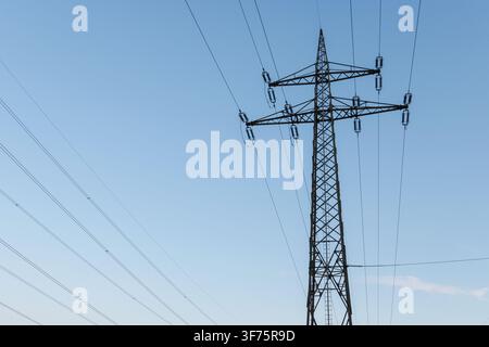 Steel tower stands tall with power lines stretching across the horizon during the day. The clear sky highlights the structure. Stock Photo