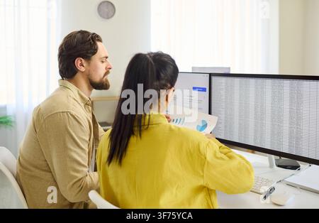 Coworkers analyzing large spreadsheets on dual monitors in bright modern office Stock Photo