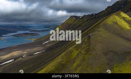 Moss-covered rhyolite mountain ridges with streaks of snow descending toward turquoise glacial lakes in Skaftárhreppur region, southeastern. Stock Photo