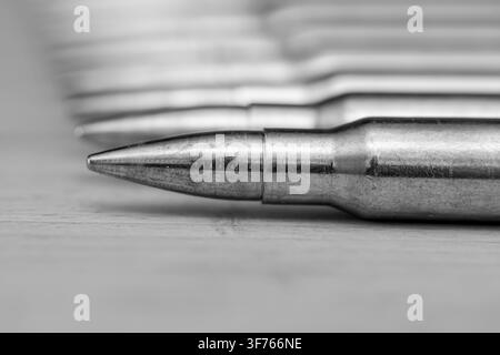 A monochrome closeup shows a metal ballpoint pen resting on a desk with blurred notebook pages in the background. Stock Photo