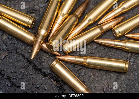 Several brass rifle cartridges are scattered across a rough dark textured surface in a close-up view. Stock Photo