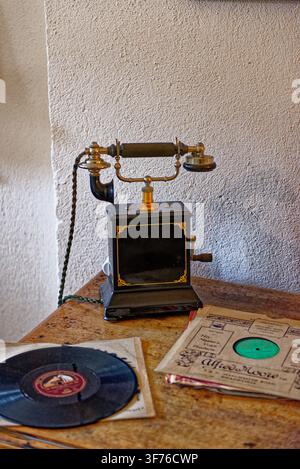 An antique magneto cradle telephone and vintage 78 RPM vinyl records sit on a rustic wooden table inside Castle Drogo, Devon, England, captured on 25. Stock Photo