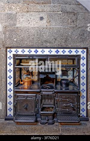 Vintage black cast iron coal stove kitchen range at Castle Drogo, Devon, England, captured on 25.08.2024, bordered by decorative blue and white cerami Stock Photo