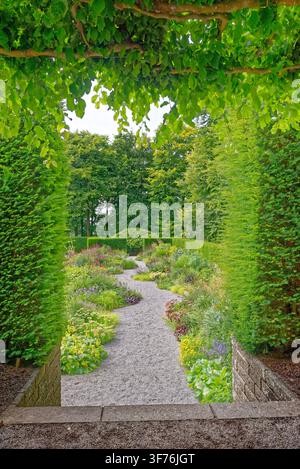 Winding gravel pathway curving through a vibrant herbaceous perennial border and manicured hedges at Castle Drogo in Devon, shot on 25.08.2024. Stock Photo