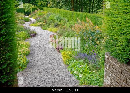 Winding gravel pathway curving through a vibrant herbaceous perennial border and manicured hedges at Castle Drogo in Devon, shot on 25.08.2024. Stock Photo