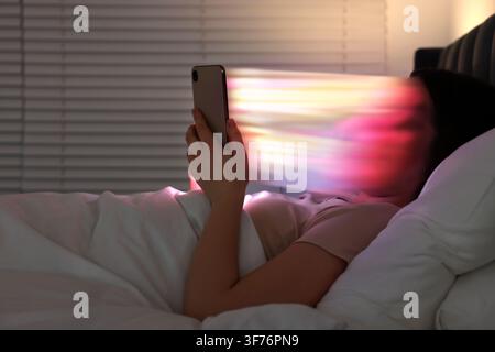 Social media addiction. Woman watching something on her phone in bed at night. Visual effect demonstrating adult person being dragged into smartphone Stock Photo