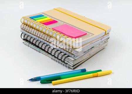 Stack of spiral notebooks with colorful pens and sticky page markers for studying Stock Photo