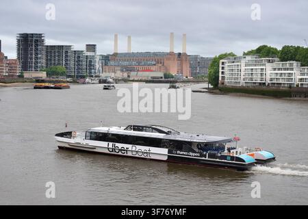 An Uber Boat Thames Clipper cruises the River Thames past London's Battersea Power Station to transport commuters and tourists along the river. Stock Photo
