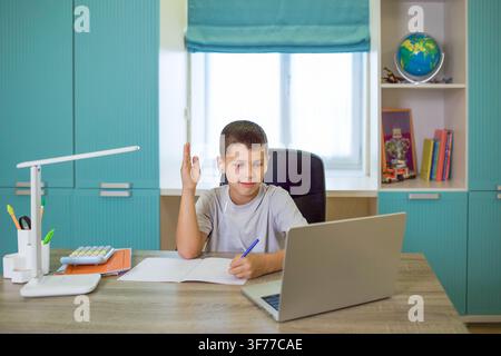 focused boy deeply engaged in online learning at wooden desk with laptop and notebook in cozy home office environment Stock Photo