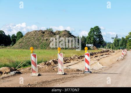 Close up view of red and white traffic warning posts on a gravel road next to large dirt mounds. Stock Photo
