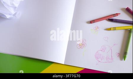 Open sketchbook with colorful crayon drawings of hearts and flowers on a bright surface, symbolizing creativity and playful imagination. Stock Photo