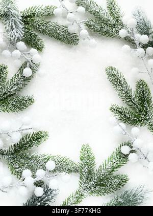 Christmas background featuring a frame of snowy pine branches and white berries on a light surface. Empty central space for text. Flat lay. Stock Photo