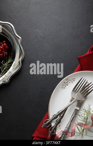 Top view of elegant silverware on plate with red napkin and pine branch on dark background. Xmas dinner concept. Copy space. Christmas concept. Stock Photo