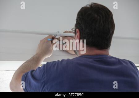 Man measuring and marking the wall above a window with pencil to drill holes for installing a curtain rod and brackets. Stock Photo