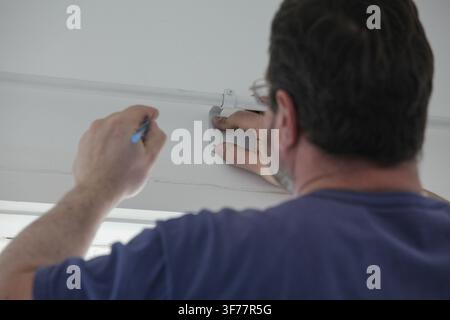 Man measuring and marking the wall above a window with pencil to drill holes for installing a curtain rod and brackets. Stock Photo