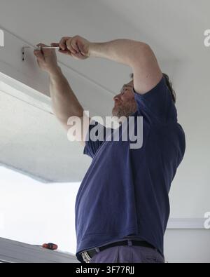 Man installing curtain rod support brackets with a screwdriver above a window during home improvement work. Practical DIY installation, home repair, r Stock Photo