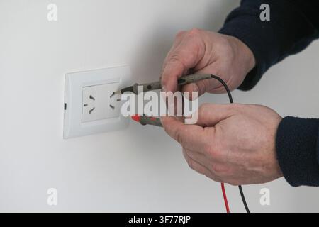 Electrician testing an electrical outlet with a digital multimeter during home electrical repair and maintenance. Modern electrical work, wiring inspe Stock Photo