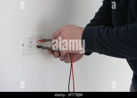 Electrician testing an electrical outlet with a digital multimeter during home electrical repair and maintenance. Modern electrical work, wiring inspe Stock Photo