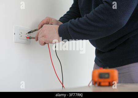 Electrician testing an electrical outlet with a digital multimeter during home electrical repair and maintenance. Modern electrical work, wiring inspe Stock Photo