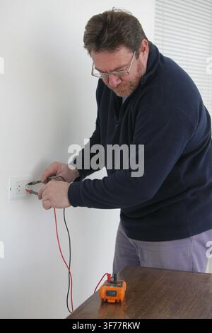 Electrician testing an electrical outlet with a digital multimeter during home electrical repair and maintenance. Modern electrical work, wiring inspe Stock Photo